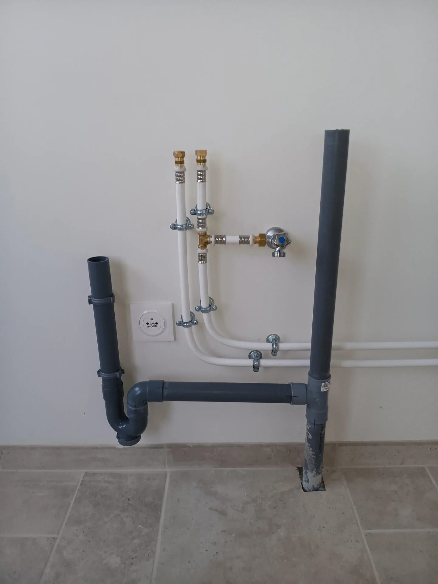 Arrivées d’eau et tuyaux d’évacuation apparents sur un mur de cuisine avant la pose des meubles.