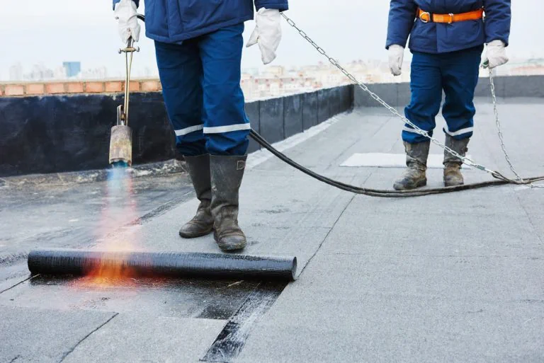 Ouvriers soudant au chalumeau un rouleau de membrane bitumineuse sur une toiture-terrasse.