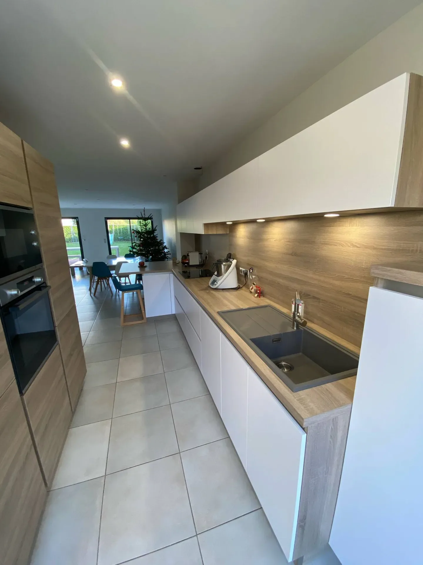 Cuisine achevée avec mobilier blanc et bois, évier, plan de travail et éclairages allumés.