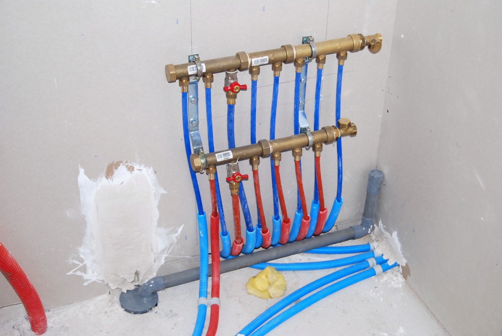 Deux collecteurs de distribution d’eau avec départs gainés en bleu et rouge et vannes visibles avant habillage du mur.